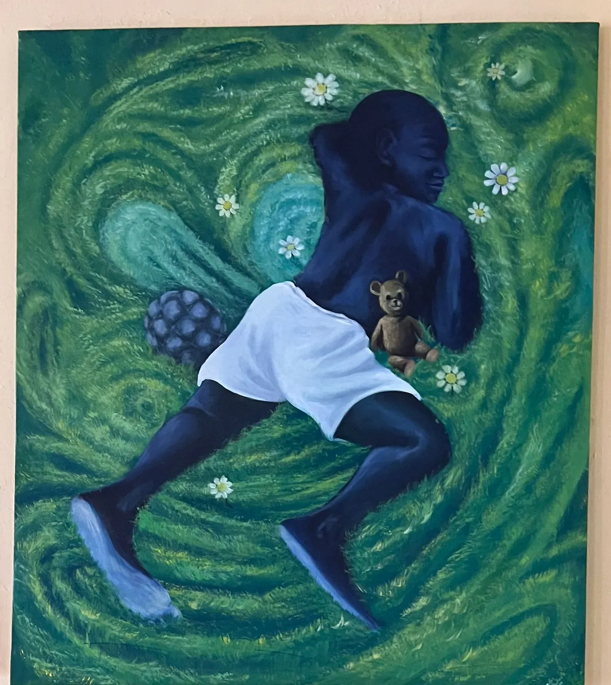 A figure lying asleep on swirling green grass in a white vest, a small toy bear tucked against their back and daisies scattered around them