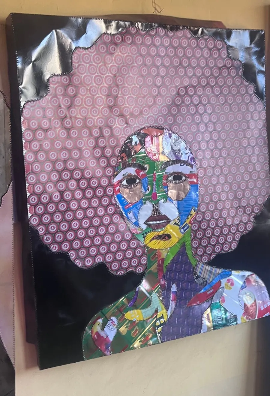 A portrait whose hair is a dense field of patterned bottle top sheet, with features cut from printed packaging and foil