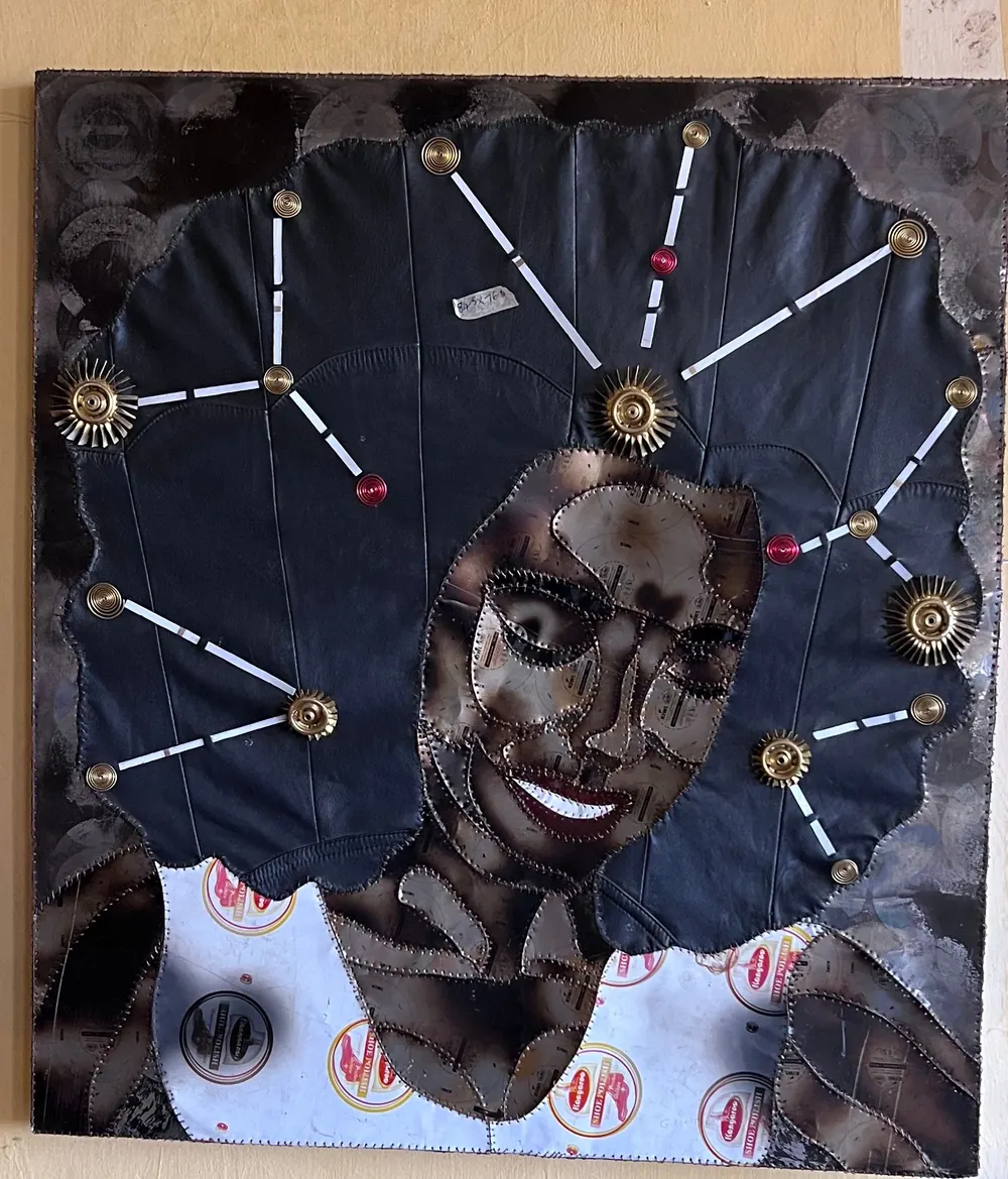 A smiling face in scorched stitched panels, surrounded by black leather threaded with white lines and studded with brass rosettes, over a strip of shoe polish labels