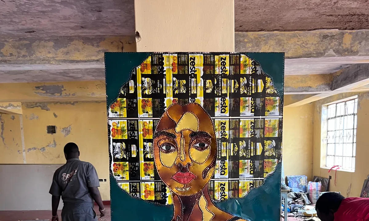 Two people working in the studio, a large stitched panel standing between them and finished work along the walls