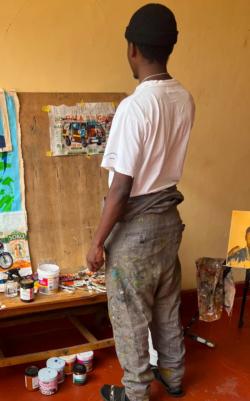 An artist at the studio board, taping up a painted snack wrapper