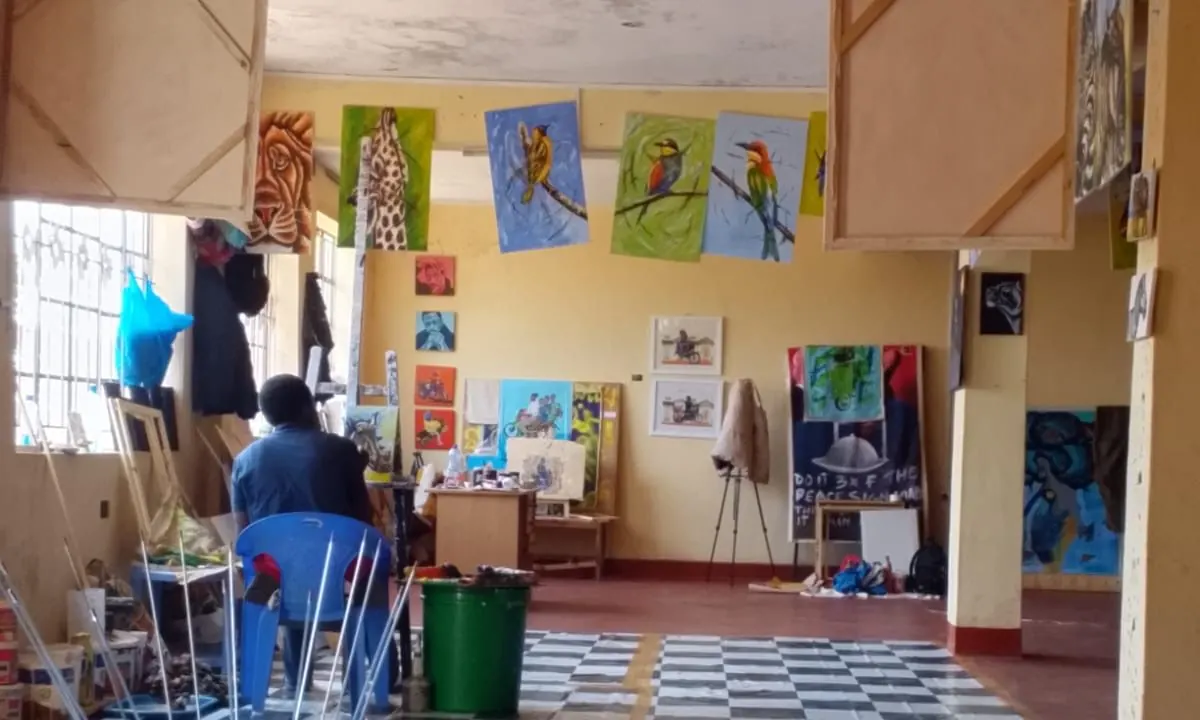 The length of the studio, someone working at the far end below paintings of birds pegged up to dry